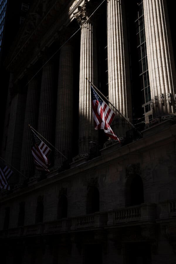 The New York Stock Exchange building seen in shadow, with tall columns and U.S. flags. 